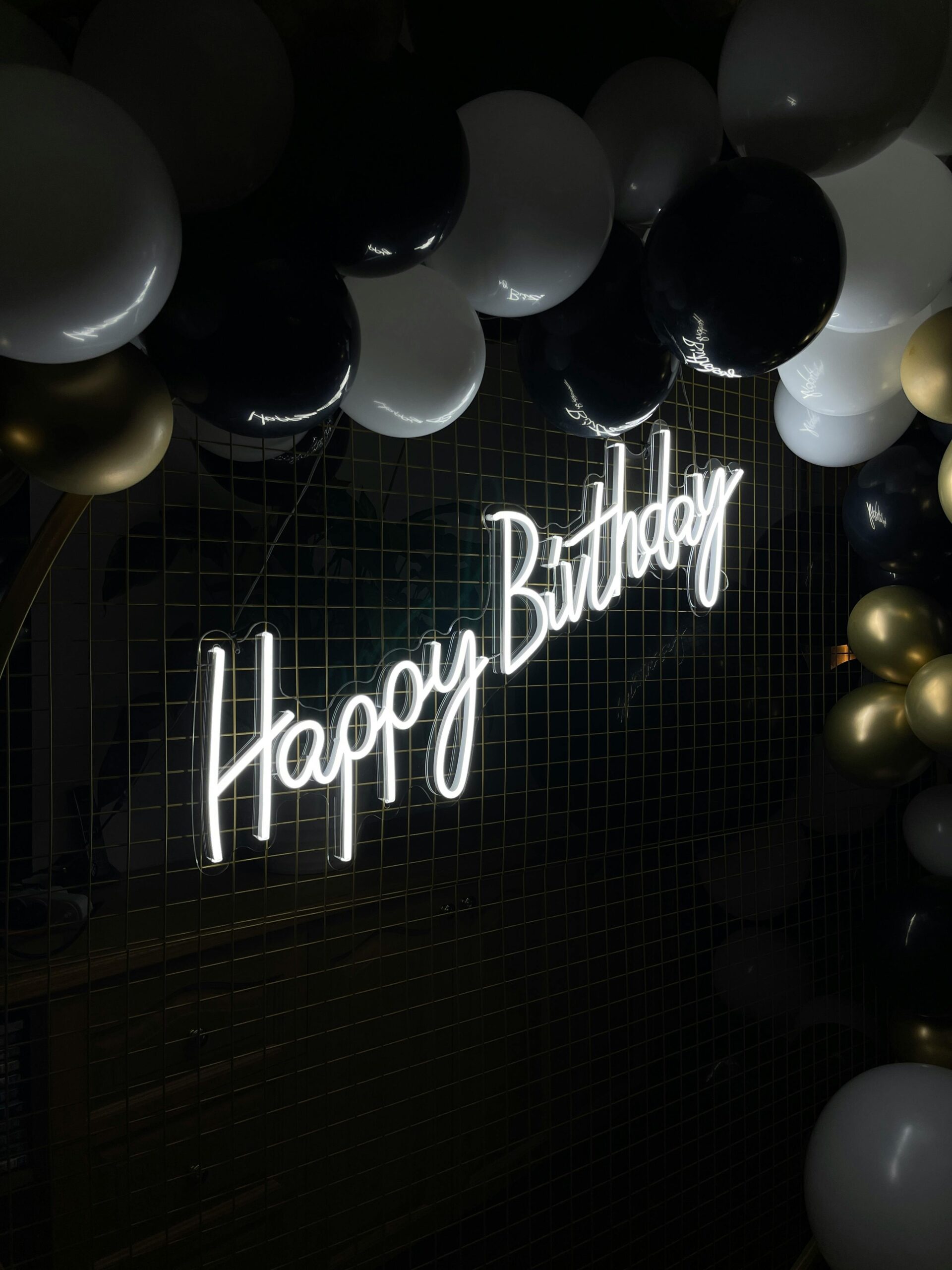 Elegant neon 'Happy Birthday' sign surrounded by black, white, and gold balloons.