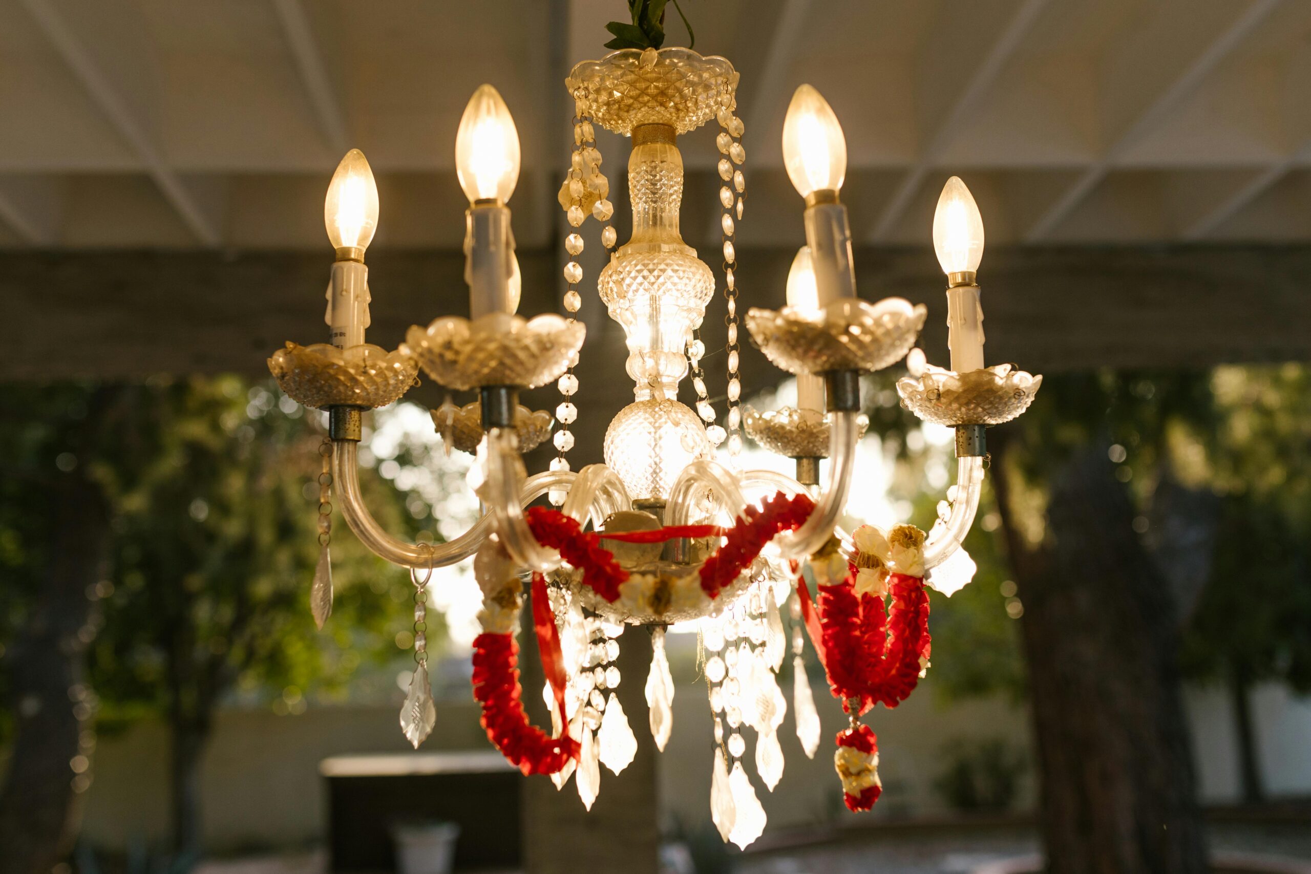An elegant chandelier adorned with red and white floral garlands hanging outdoors in a serene setting.